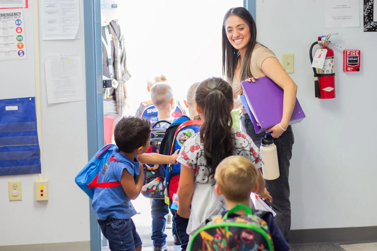 A smiling woman leads a group of students outside a classroom